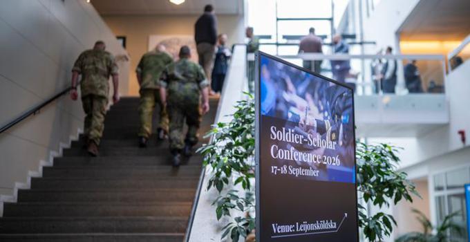 Militärer som går uppför en trappa samt skylt till konferens i FHS entré. 