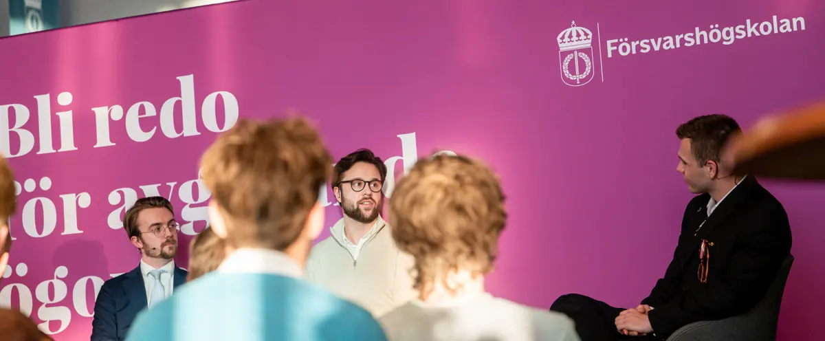 En grupp människor som sitter framför en rosa vägg.