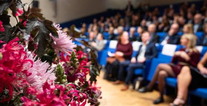 föreläsningssal fylld med festklädda personer och blommor i förgrunden
