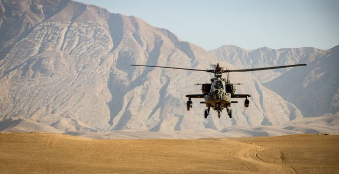 En militärhelikopter i luften framför berg i bakgrunden. 