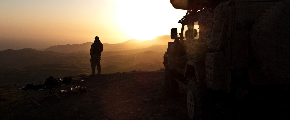 Soldat spanar mot soluppgången bredvid militärfordon.