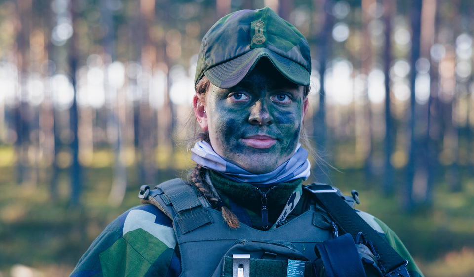Kvinnlig kadett med kamouflagesmink i ansiktet på övning i skogsmiljö.
