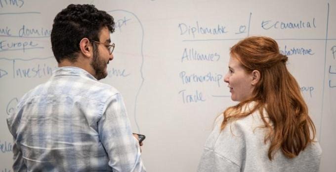 Khalil Talhaoui och Emelie Moregård talking to each other standig in front of a whiteboard-screen.