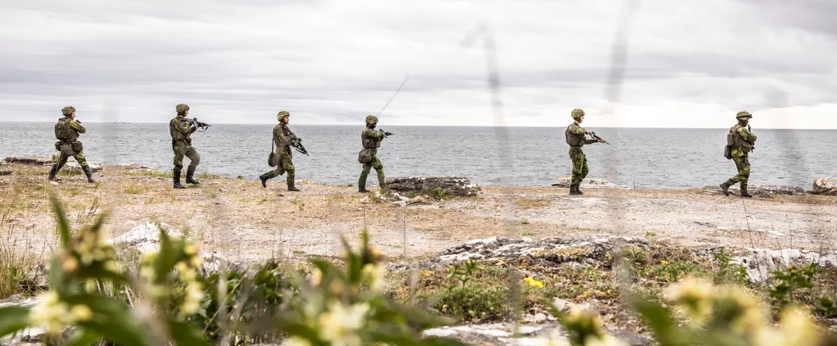 En grupp soldater som går över ett fält intill havet.