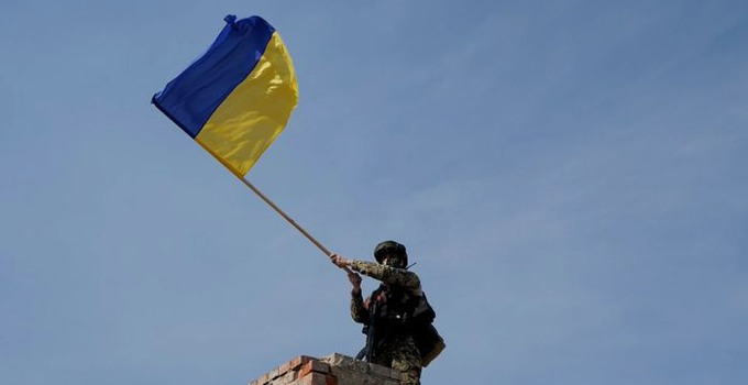 Ukrainsk soldat håller i den ukrainska flaggan mot en blå himmel.