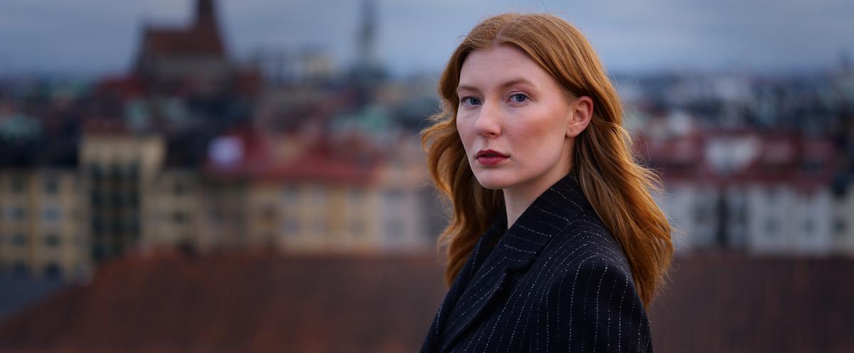 Kvinnlig student tittar in i kameran stående upp på Försvarshögskolans tak.