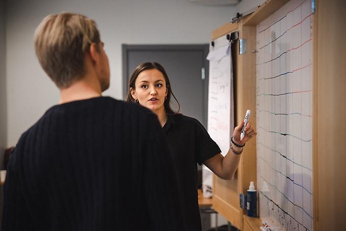 Studenten Fredrika Stense står vid en whiteboardtavla och pratar med en annan student.