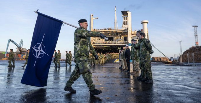 Militär som bär en Nato-flagga framför en båt. 