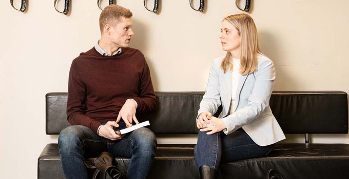 Två studenter på en soffa under värjorna i entréhallen.
