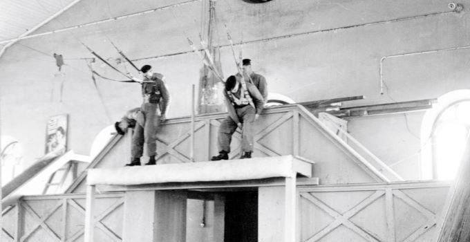 Soldater tränar fallskärmshoppning inomhus på 1950-talet.