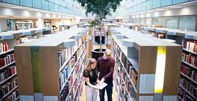 A couple of people standing in a library.