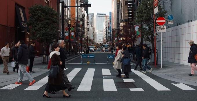 Bilden visar kvinnor och män som går över ett övergängsställe i en japansk stad. 