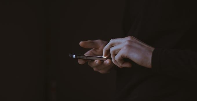 Närbild på hand som håller i en smart mobil mot en mörk bakgrund. 