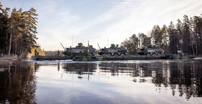 Soldater transporterar militärfordon över ett vattendrag.