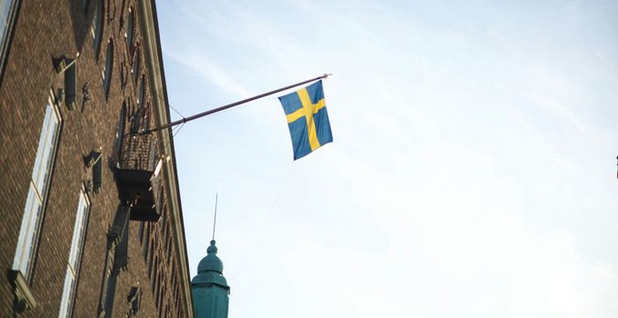 Svensk flagga som hänger från en husfasad mot blå himmel.