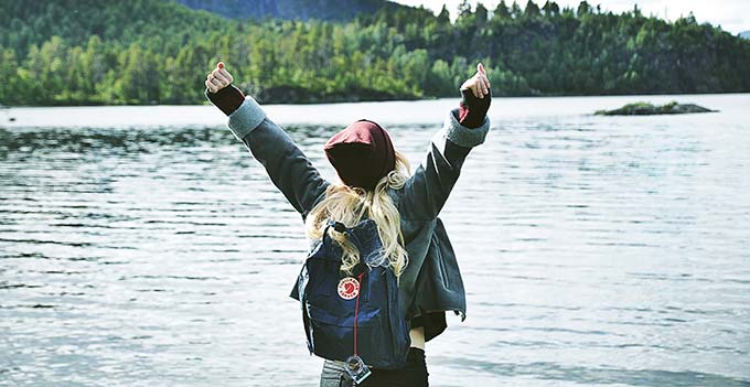 Kvinna sträcker upp armarna i luften vid en sjö.