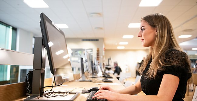 En kvinna som sitter vid ett skrivbord och använder en dator.