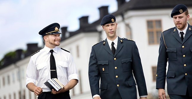 Tre män i militäruniformer som går framför en byggnad.