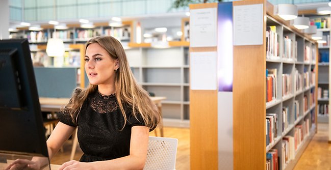 En kvinna som sitter vid en dator på ett bibliotek.