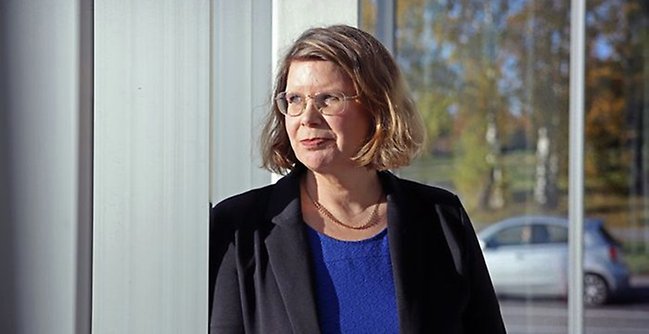 Campus totalförsvars föreståndare Arita Holmberg står vid fönster som speglar träd och bil i bakgrunden