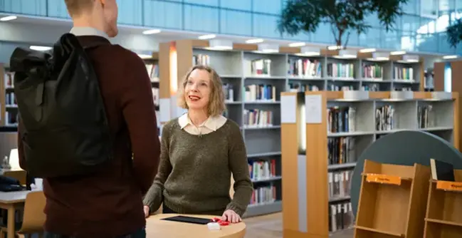 A woman talking to a man in a library.