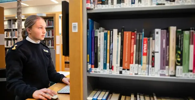 A woman standing in front of a computer in a library.