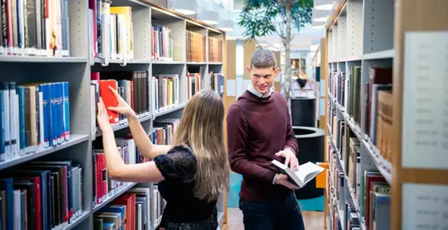 A man and a woman looking at books in a library.